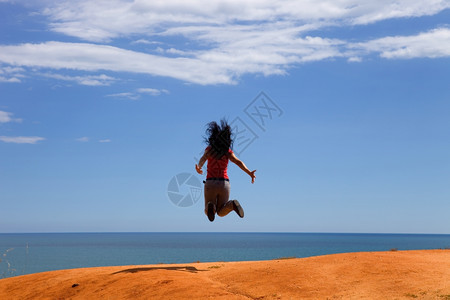 年轻女子在海岸张开双臂跳跃图片