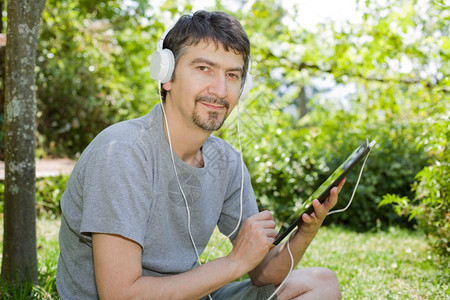 青年男子在户外持有带耳机的平板电脑图片