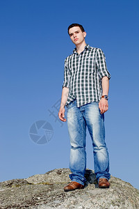 年轻散工在岩石顶上天空是背景图片