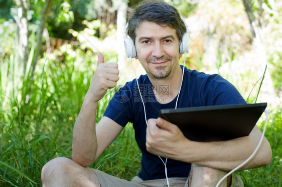 青年男子在户外持有带耳机的平板电脑图片