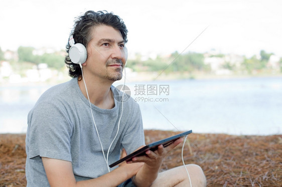 青年男子在海滩上拿着带耳机的平板电脑图片