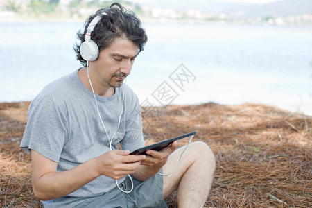 青年男子在海滩上拿着带耳机的平板电脑图片