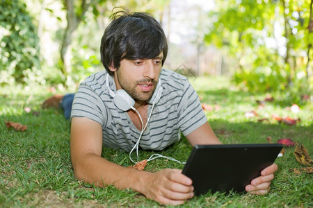 年轻人在公园户外与平板电脑一起放松听音乐和耳机图片
