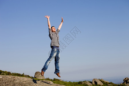 年轻快乐的男孩在一个巨大的岩石跳跃图片