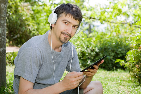 青年男子在户外持有带耳机的平板电脑背景图片