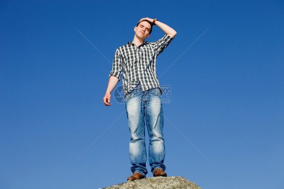 年轻散工在岩石顶上天空是背景图片