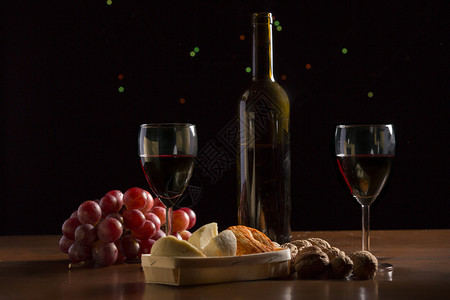 以黑底木制桌边的葡萄和坚果制成的酒奶酪坚果和葡萄图片
