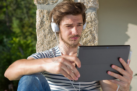 青年男子在户外用耳机收听音乐图片