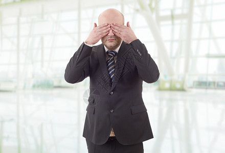 英俊的商人遮着眼睛无视一切在办公室背景