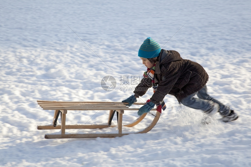 小男孩把雪上山坡推向图片