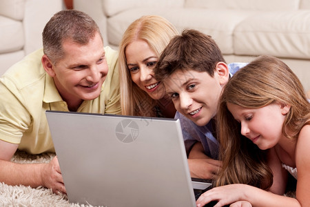 四口幸福家庭在客厅的地毯上放松时浏览笔记本电脑图片