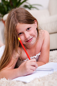 在客厅用铅笔和记本微笑的年轻女孩看着你图片