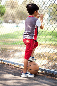 年轻篮球选手的后视镜握着球在腿下透过栅栏看球图片