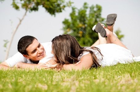 快乐的年轻情侣躺在草地上互相看着对方图片