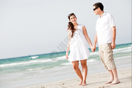 年轻夫妇握手在海滩上行走的全图象图片