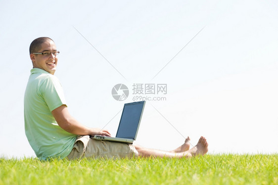 一名青年男子用笔记本电脑坐在公园的草地上图片