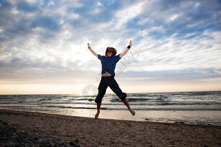 快乐的年轻人在日落时海滩上跳跃图片