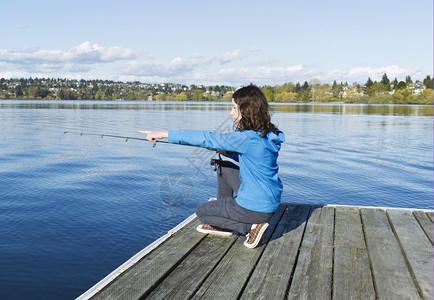 女孩在从木船坞捕鱼时指向在湖边喂鱼图片