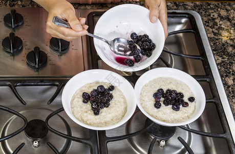 将蓝莓添加到燕麦早餐中在炉灶顶端的白碗中图片