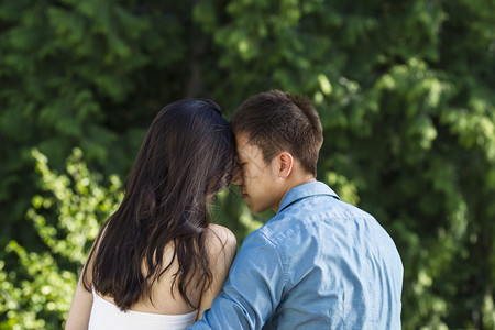 一对年轻成夫妇触摸前额到的横向照片背景有绿树图片