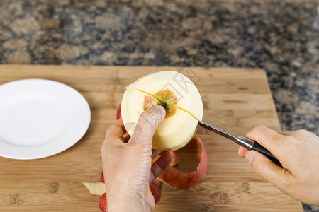 女手用刀割竹砍板白盘和本底石头顶的刀切割鲜皮苹果的横向照片图片