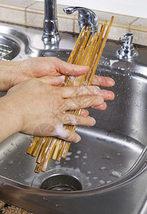 垂直照片女手用肥皂水清洗竹筷子和肥皂水以及厨房槽和背景龙头图片