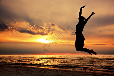 快乐的女人在日落时海滩上跳跃快乐的女人成功能量福利理念图片