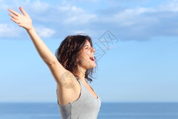 高举手的迷人女向沙滩的风喊叫背景是海和蓝天空图片素材