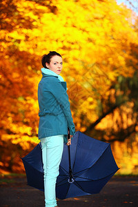 秋天的生活方式概念在秋季公园用蓝伞行走的心身年轻女子黄色金叶背景图片
