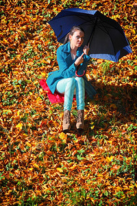 秋天的生活方式概念在秋天公园用蓝伞放松的心身年轻女孩金色的叶子背景图片