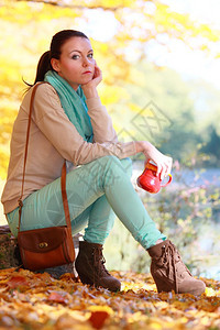 秋天公园中深思熟虑的年轻女士在享受热饮咖啡或茶拿着红杯加热饮喝的休闲娱乐中放松黄叶背景图片