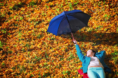 秋天的生活方式概念在秋天公园用蓝伞放松的心身年轻女孩金色的叶子背景图片