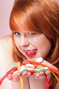 年轻快乐的红发女郎带着糖多彩的果冻甜点手握着粉红背景图片