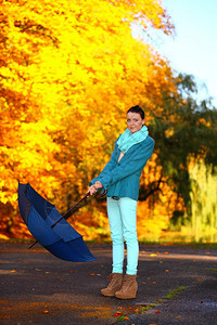 秋天的生活方式概念在秋季公园用蓝伞行走的心身年轻女子黄色金叶背景图片
