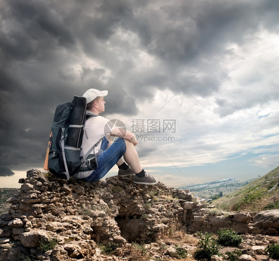 坐在云层下岩石上的观光客图片