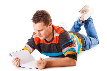 躺在地板上阅读一本书的全年男学生为以白人背景孤立的考试做准备图片