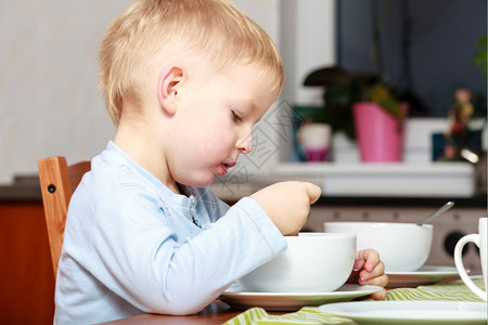 童年快乐金发小男孩吃玉米片饭桌上吃牛奶早餐麦片图片