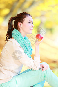 秋天的生活方式概念和谐自由偶然的年轻女孩在秋季公园放松吃红苹果金色的叶子背景图片