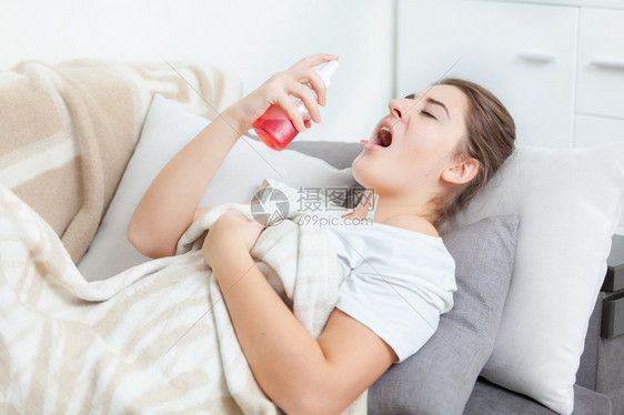 躺在起居室并使用喉喷雾剂的患病妇女图片