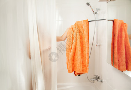 淋浴中的女人从钩子上摘下橙色毛巾图片