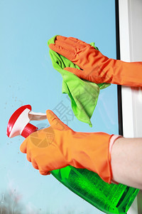 用绿色抹布和喷洒洗涤剂用橙色手套清洗窗图片