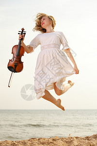 疯狂的金发女音乐情人在沙滩上骑小提琴跳跃时快乐的金发女音爱好者的概念图片