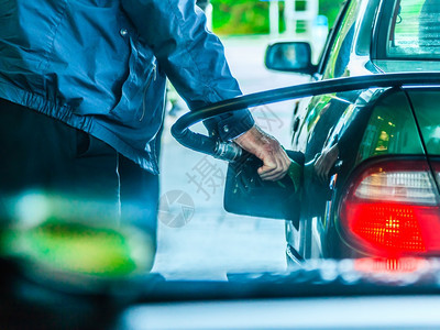 男子在加油站用煤气或汽重新装满车在户外持有燃料泵图片