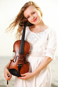 金发女孩音乐情人的肖像带着小提琴在海滩上图片