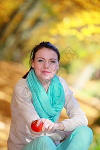 秋天的生活方式概念和谐自由偶然的年轻女孩在秋季公园放松吃红苹果金色的叶子背景图片