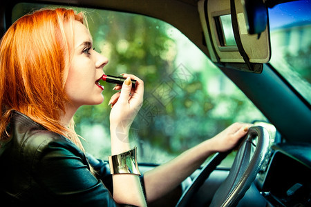 年轻女司机红发少在开车时嘴唇上涂油图片