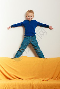 满脸笑的金发男孩站在沙发上玩耍图片