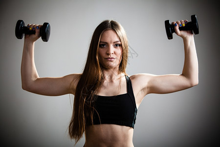 身体健康的女孩身体健康的女人抬起哑铃的重量用锻炼运动用哑铃训练肩部肌肉灰色背景图片