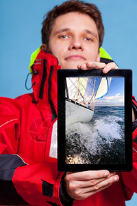 穿风衣的人拿着有游艇帆船照片的皮卡水手展示了屏幕板触摸梦想着游艇航行技术和游轮图片
