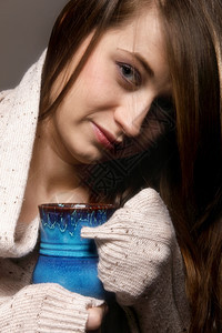 一位美丽的caucasian女人的近身拿着一杯漂亮的蓝温暖饮料灰色背景图片
